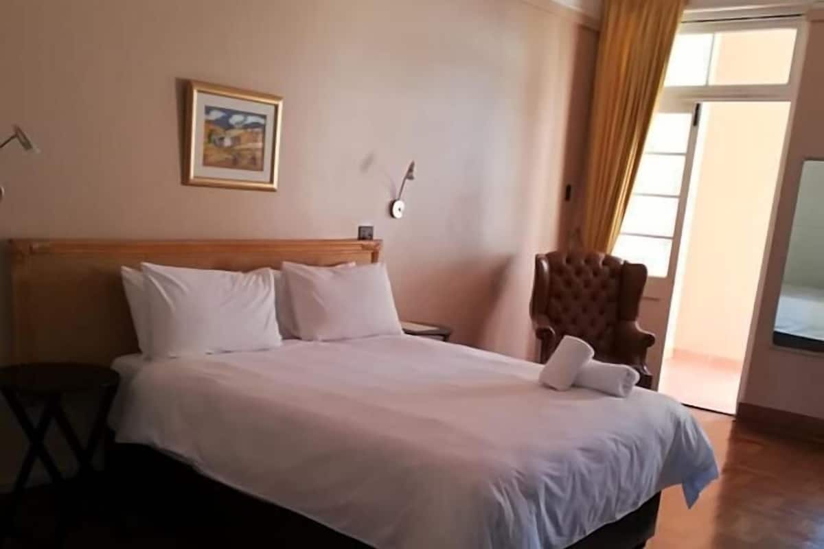 Ein ordentlich bezogenes Bett mit weißen Leinen in einem Hotelzimmer mit Holzboden und einem großen Fenster mit Vorhängen.