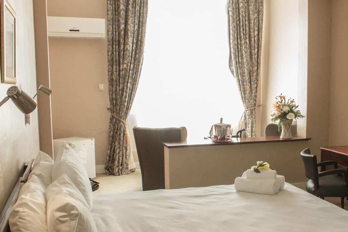 Ein Hotelzimmer mit Bett, Schreibtisch, Stuhl, Spiegel und einem Fenster mit Vorhängen.