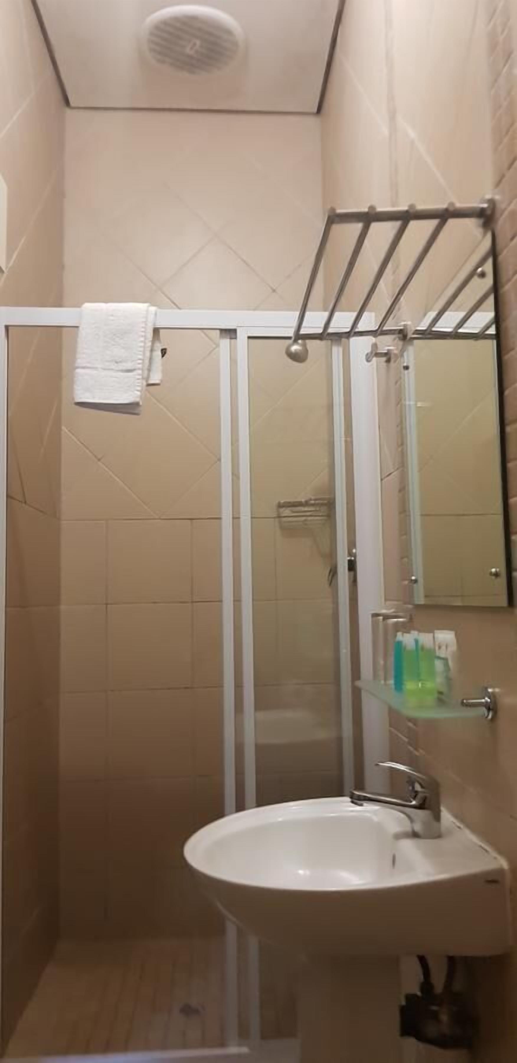 A bathroom with a glass shower enclosure, a white sink, and a glass shelf with toiletries.