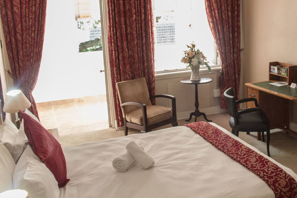 Ein Hotelzimmer mit Bett, zwei Stühlen, Schreibtisch, Lampe und einem Vorhangfenster.
