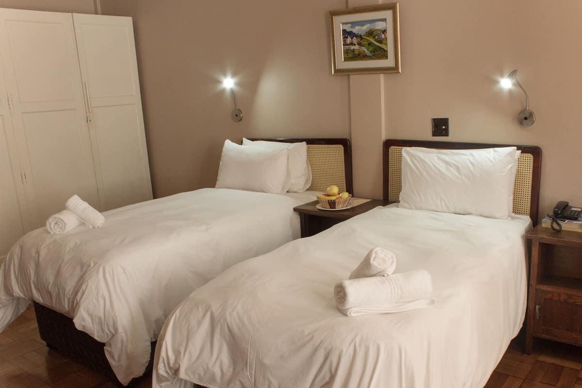 Ein Hotelzimmer mit zwei Betten, jeweils mit weißer Bettwäsche und Handtüchern, einem Nachttisch mit Lampe und einem Bild an der Wand.