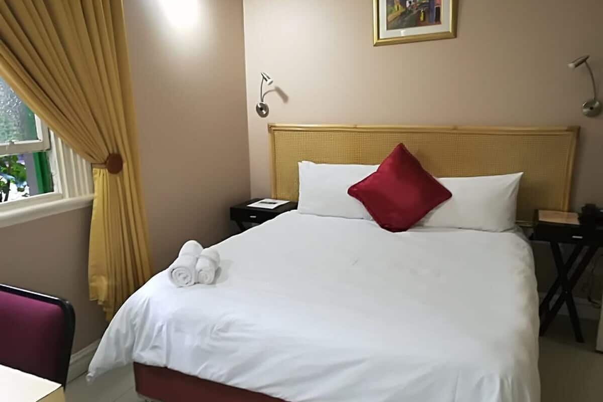 Ein Hotelzimmer mit Bett, Nachttisch, Stuhl und einem Fenster mit Vorhängen.
