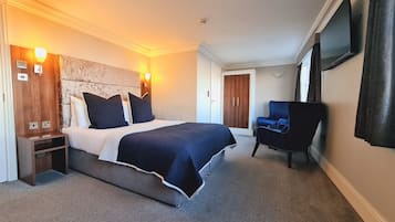A hotel room with a large bed, bedside tables, a chair, a TV, and a wardrobe.