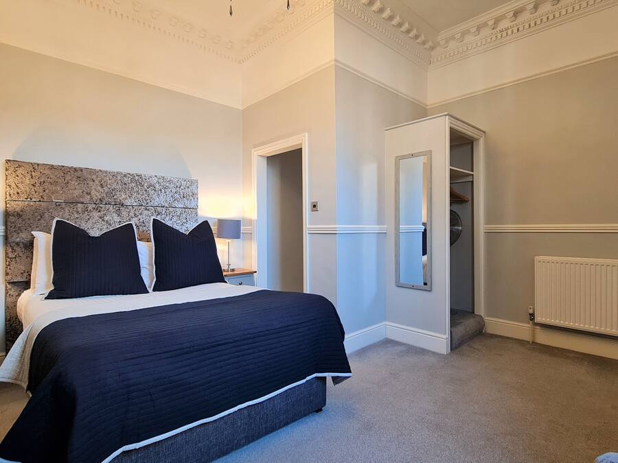 A neatly arranged bedroom with a large bed, bedside lamps, a dresser, and a radiator.
