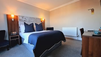 A hotel room with a bed, bedside tables, a desk, and a chair. There is a telephone on one of the bedside tables.