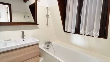 Une salle de bain moderne avec un double vasque, une baignoire et une fenêtre ornée de rideaux en dentelle.