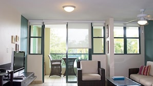 Een woonkamer met een televisie, een bank, een salontafel en een balkon met stoelen.