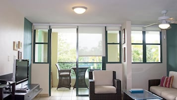 Una sala de estar con televisor, sofá, mesa de centro y balcón con sillas.