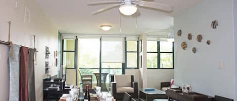 A dining area with a table set for four, a ceiling fan, and a view of the outdoors through large windows.