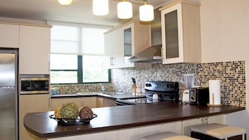 Una cocina moderna con gabinetes blancos, una estufa negra, un microondas y un lavamanos. Hay una ventana que proporciona luz natural y un cuenco decorativo sobre la encimera.