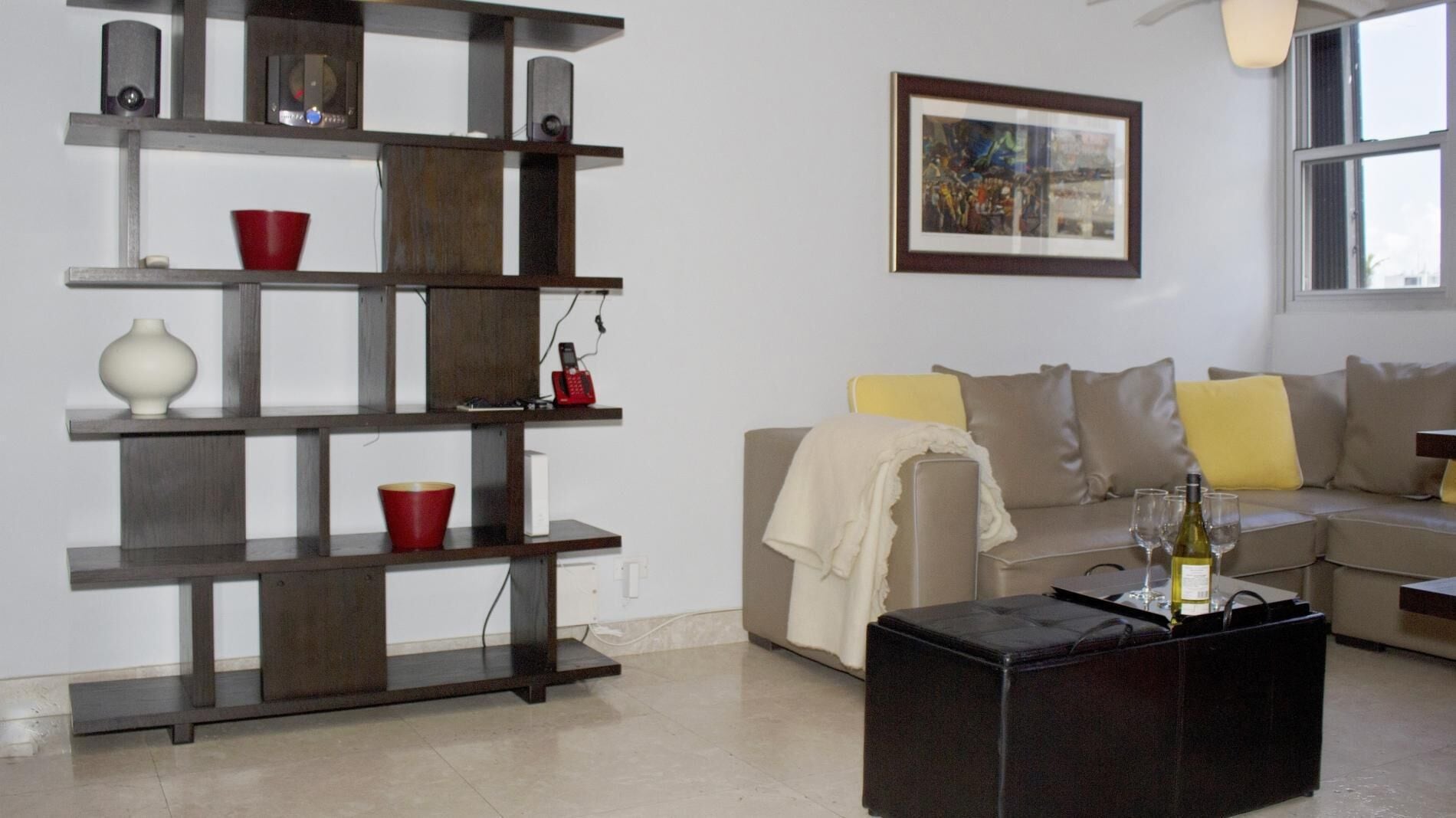Una sala de estar con un sofá, una mesita de centro con copas de vino, una estantería y un cuadro enmarcado en la pared.
