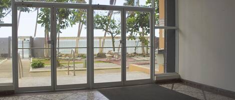 Una habitación con puertas de vidrio amplias que dan a un espacio exterior con vista a palmeras y una playa.