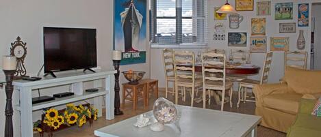 Sala de estar com televisão, mesa de jantar com cadeiras, sofá e diversos enfeites nas paredes.