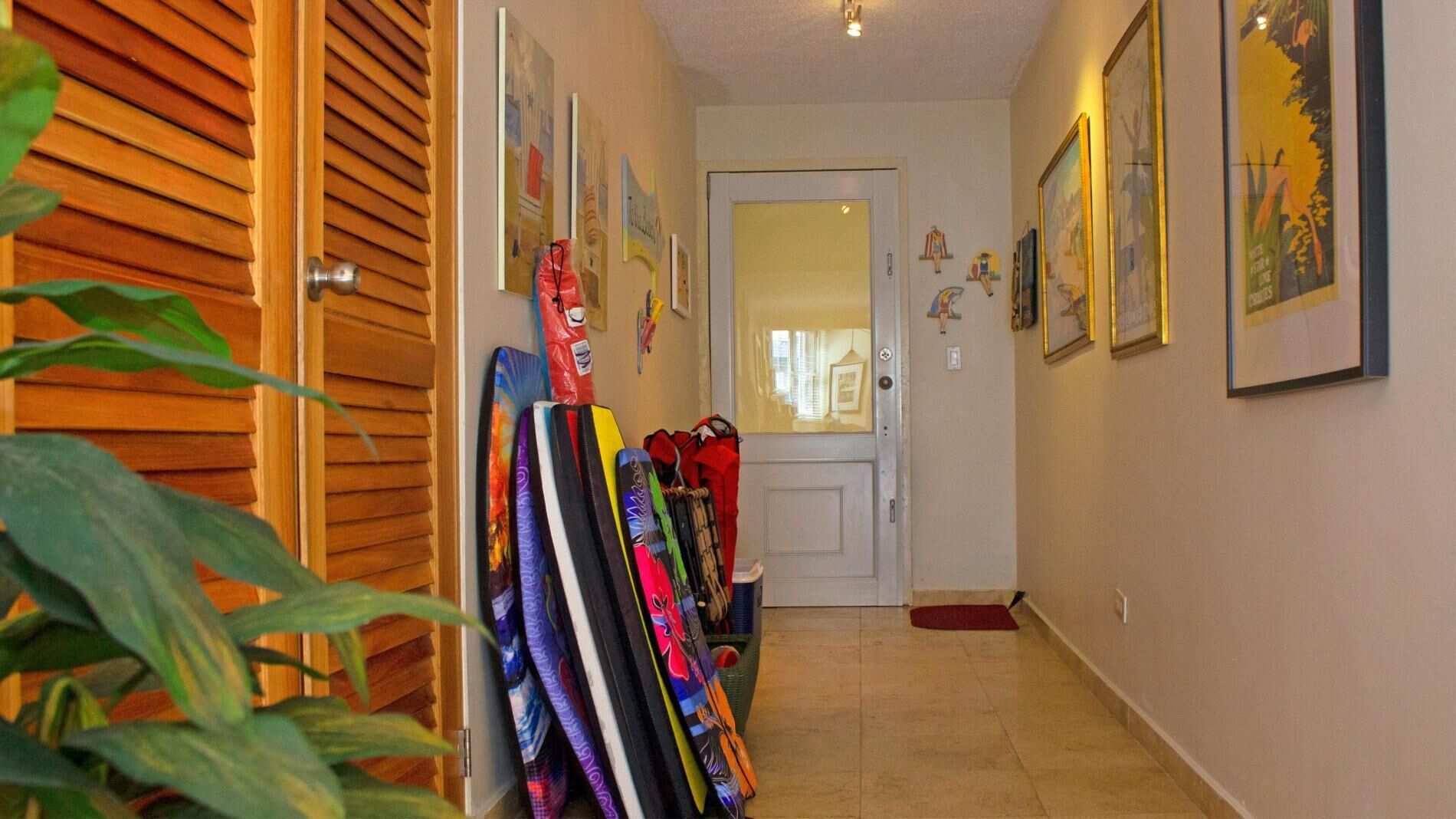 A hallway with a wooden door, a coat rack with colorful items, and framed pictures on the walls.