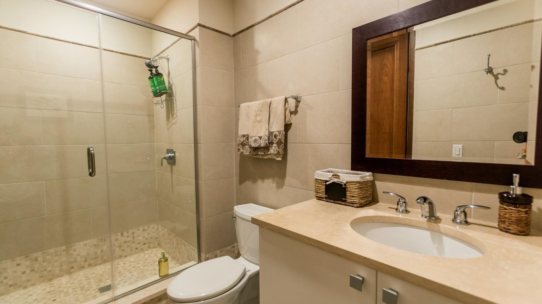 Ein Badezimmer mit Glasdusche, Toilette, Waschbecken mit Spiegel und einem kleinen Korb auf der Ablagefläche.