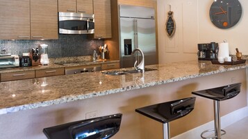 Una cocina moderna con encimeras de granito, electrodomésticos de acero inoxidable y taburetes de bar.