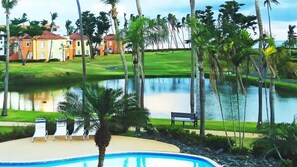 A swimming pool with lounge chairs, a bench, and a pond with palm trees.