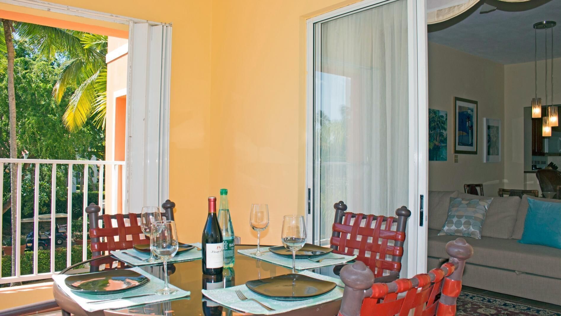 Un comedor con una mesa preparada para cuatro personas, una botella de vino y dos copas de vino vacías.
