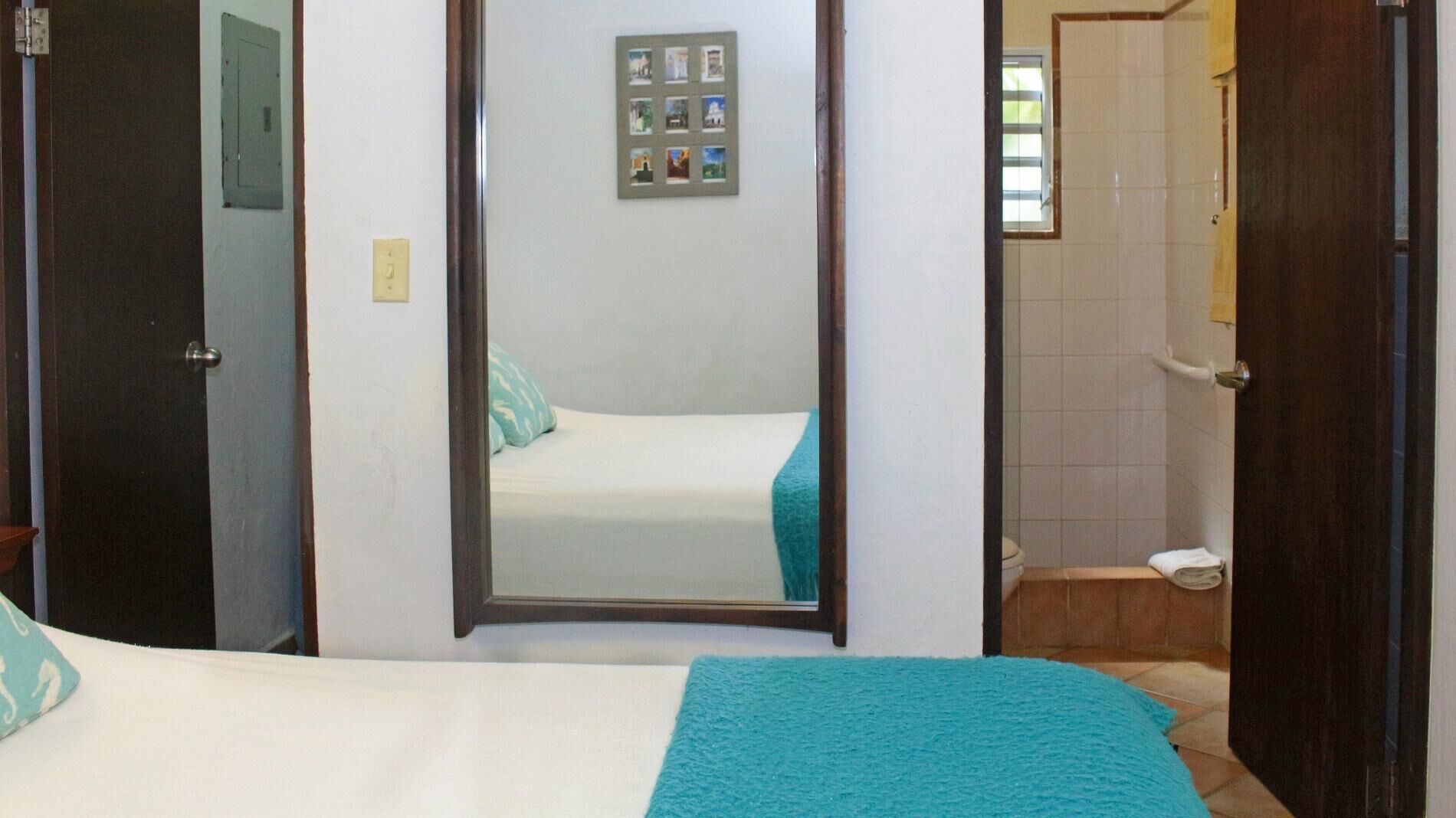 A bedroom with a bed, a mirror, and a bathroom visible through an open door.