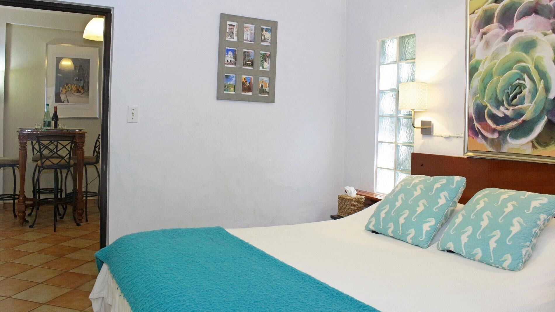 Een hotelkamer met een bed, een kleine tafel met stoelen, een lijst met foto's aan de muur en een groot schilderij boven het bed.