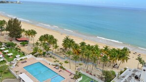 A beach view with a swimming pool, palm trees, and beach umbrellas. - Isla Bella (Carolina)
