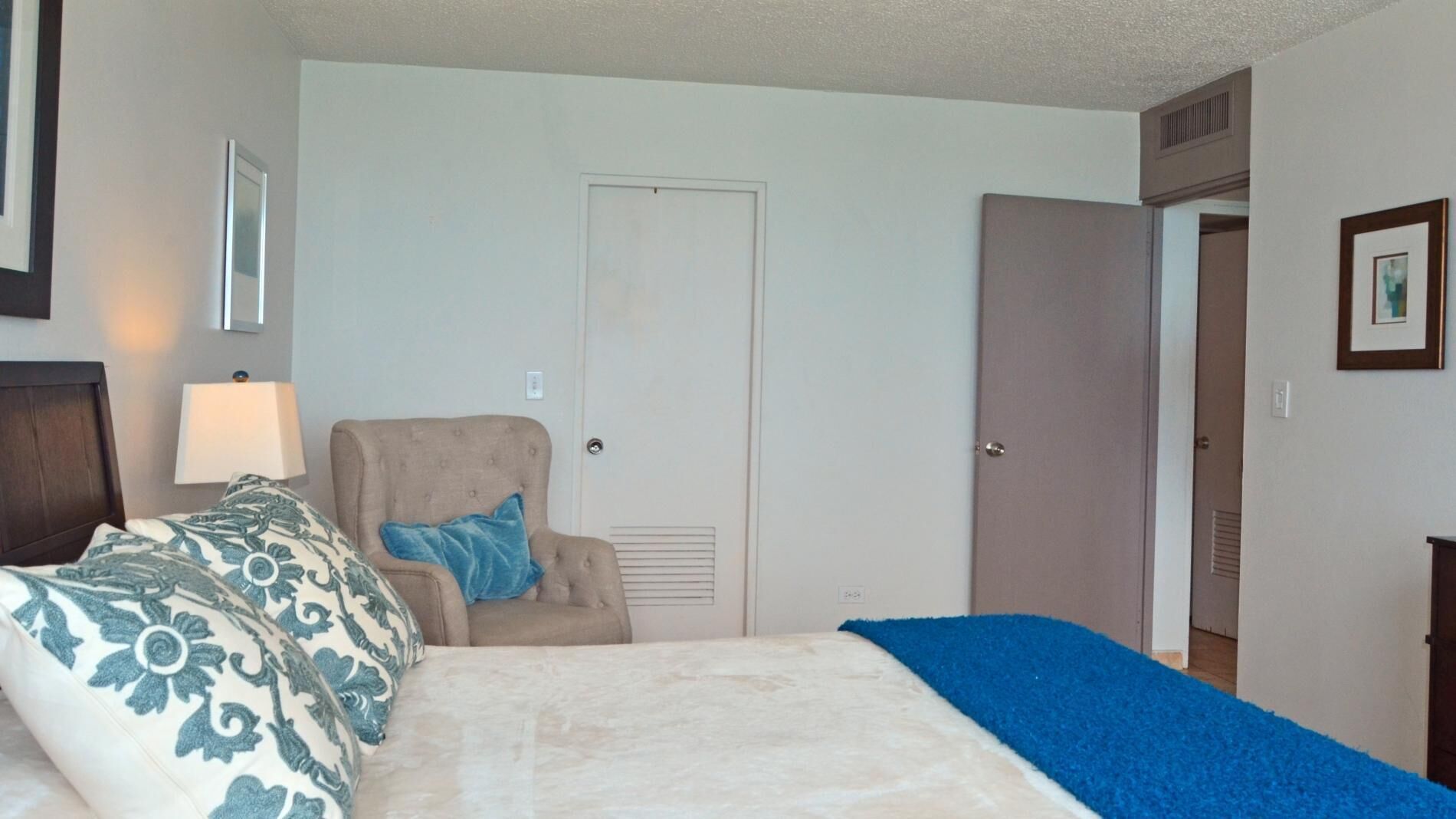 A bedroom with a bed, a chair, a door, and a wall-mounted lamp.