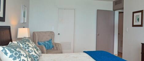 A bedroom with a bed, a chair, a door, and a wall-mounted lamp.