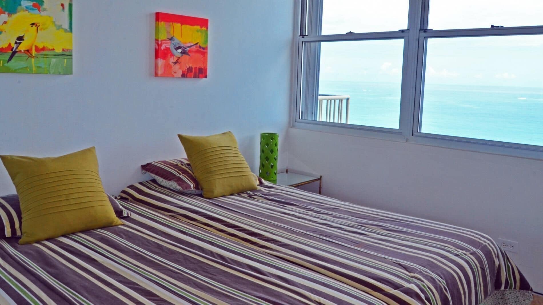Une chambre à coucher avec un lit, deux oreillers, un vase vert et deux tableaux accrochés au mur.
