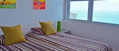 A bedroom with a bed, two pillows, a green vase, and two paintings on the wall.