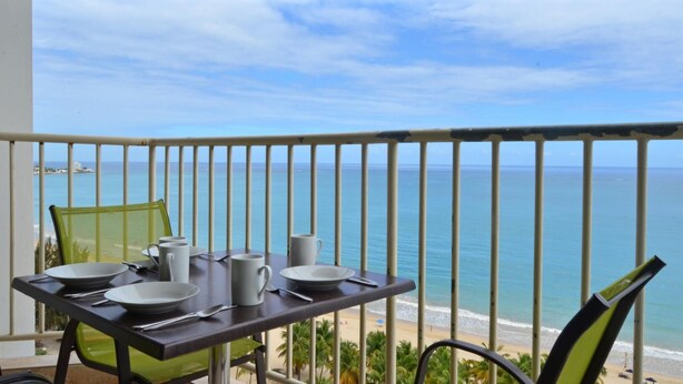 A balcony with a table set for two, overlooking a beach and the ocean. - Isla Bella (Carolina)