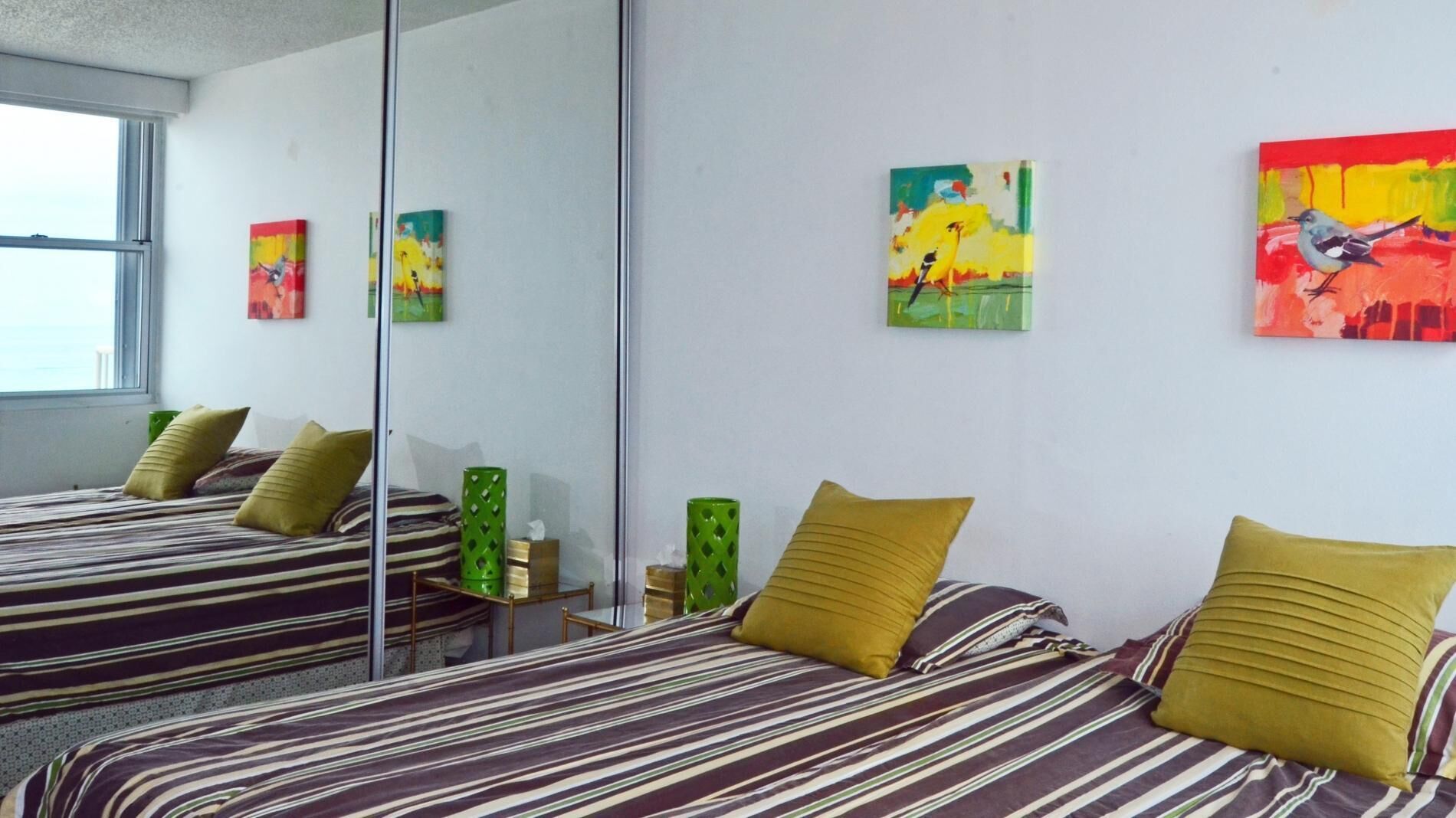 A hotel room with two beds, striped bedding, and colorful artwork on the walls.