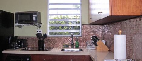 A kitchen with a microwave, sink, and window with blinds.