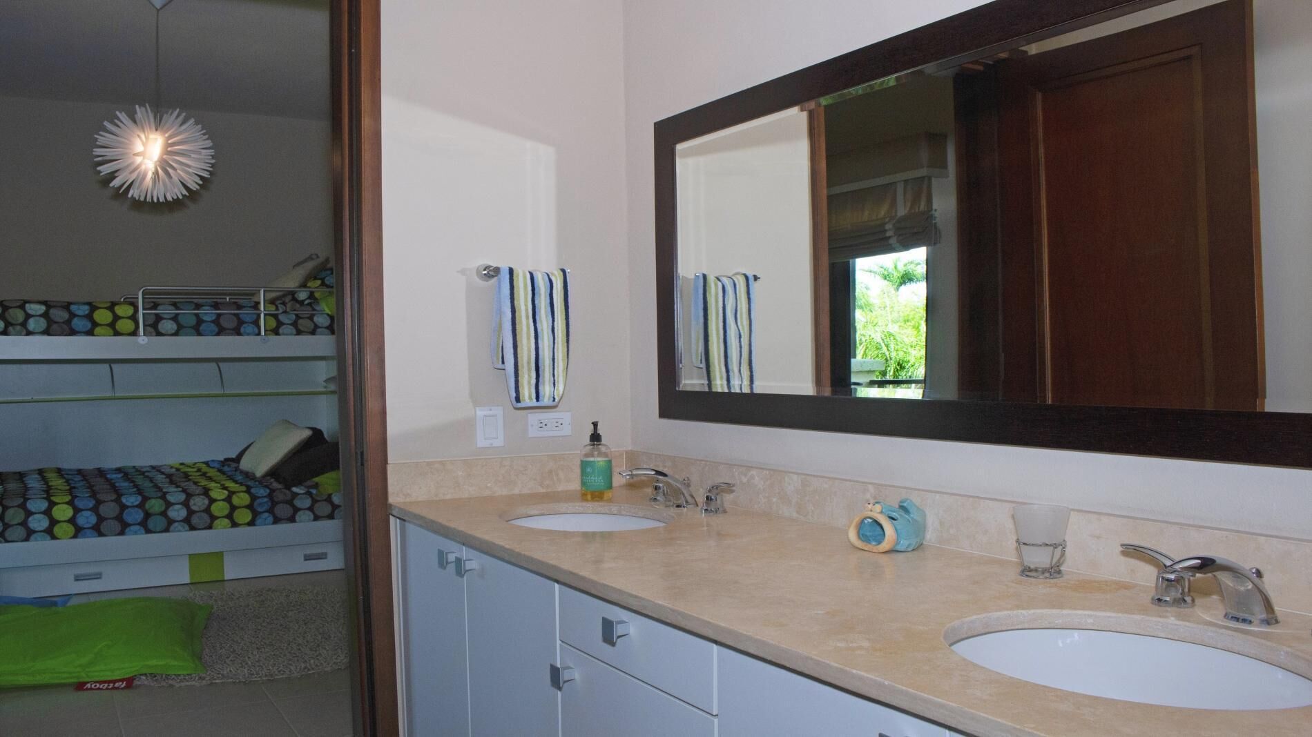 Une salle de bain moderne avec deux lavabos, un grand miroir et un luminaire au plafond au design original.