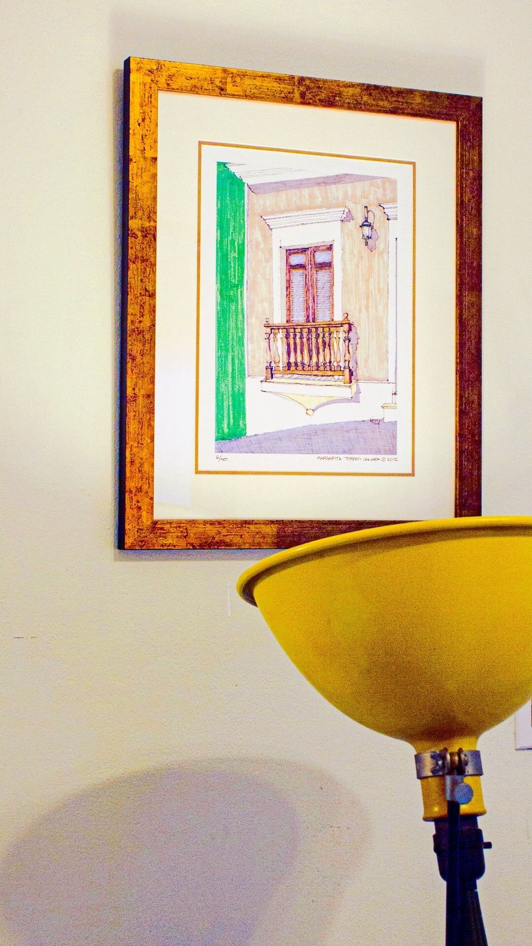 A framed artwork of a building with a balcony, mounted on a wall.