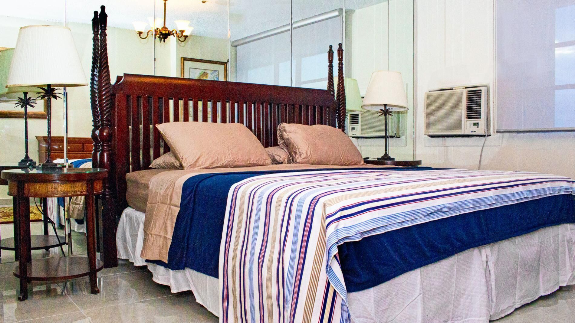 A neatly made bed with a striped bedspread, a wooden headboard, and two bedside lamps.