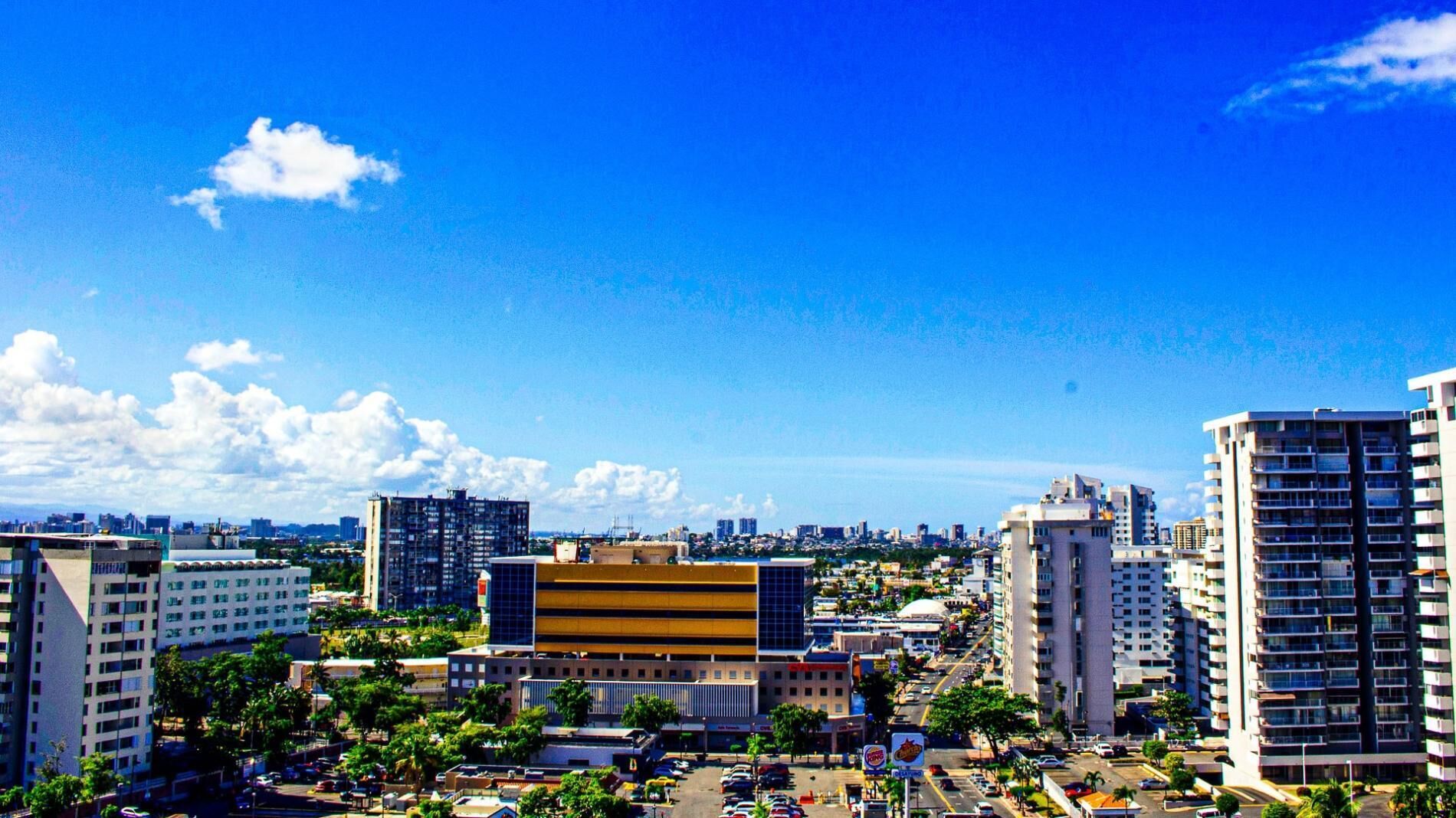 Une vue urbaine avec des immeubles modernes de grande hauteur, un bâtiment jaune au centre et un ciel bleu dégagé.