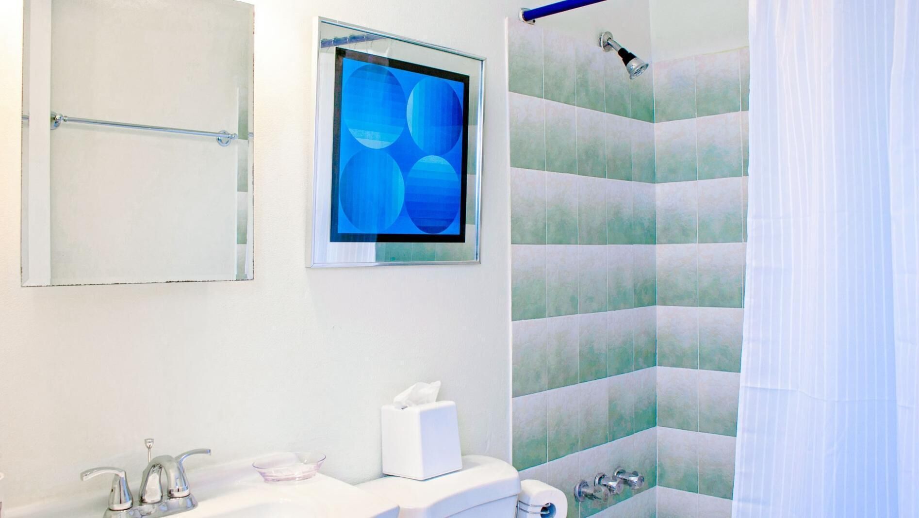 A modern bathroom with a white sink, a glass-topped basin, a toilet, a shower with a glass door, and a framed abstract artwork on the wall.
