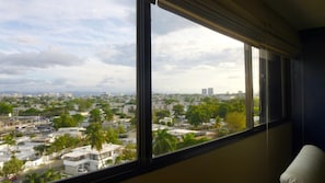 Enjoy a city view from the room's large window, featuring a partial view of the city's residential buildings and lush greenery.