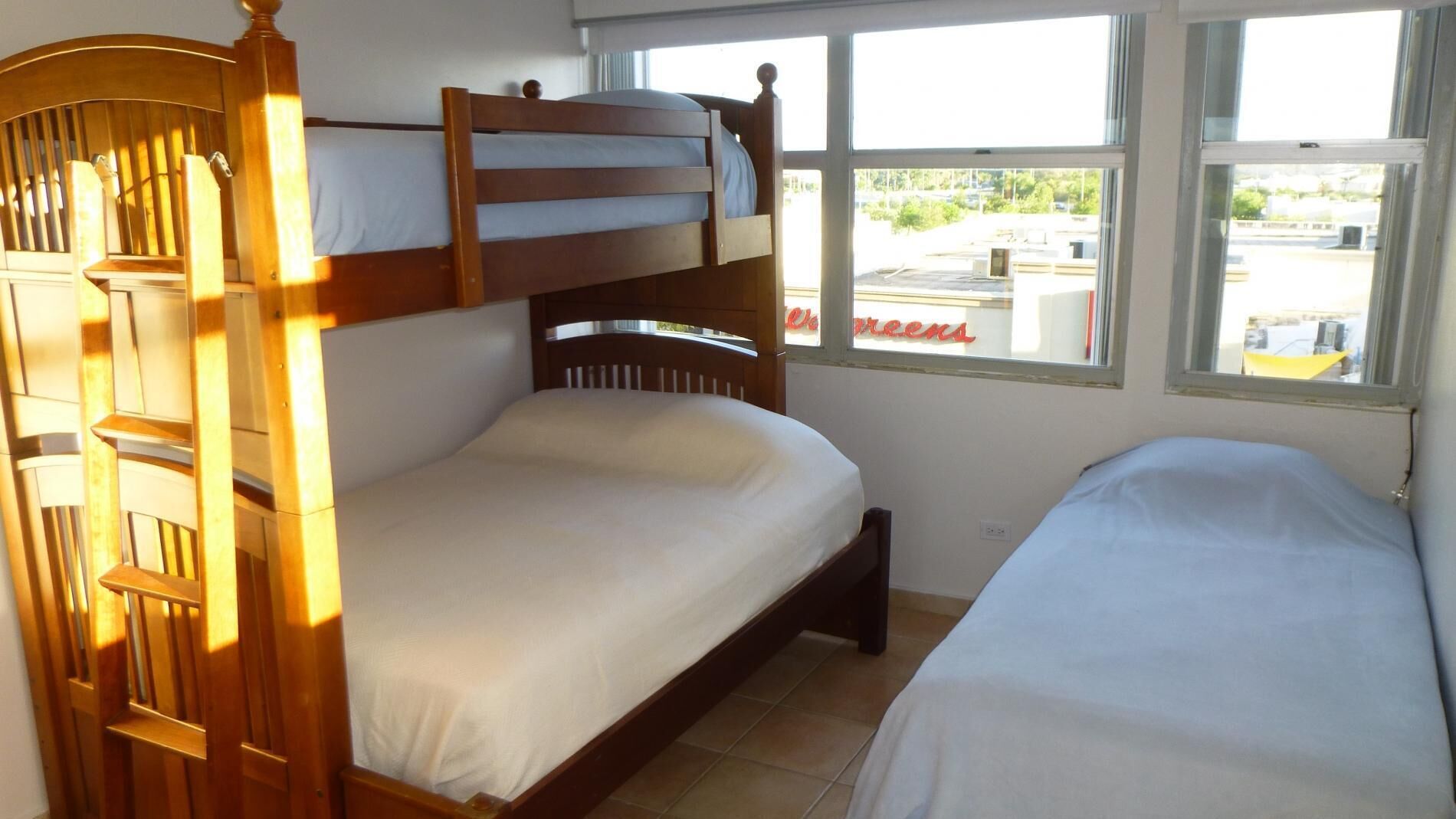 A bunk bed room with a wooden headboard, a window with a view of a parking lot, and a small table.