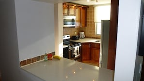 Een kleine keuken met houten kastjes, een roestvrijstalen oven, een magnetron, een koffiezetapparaat en een koelkast.
