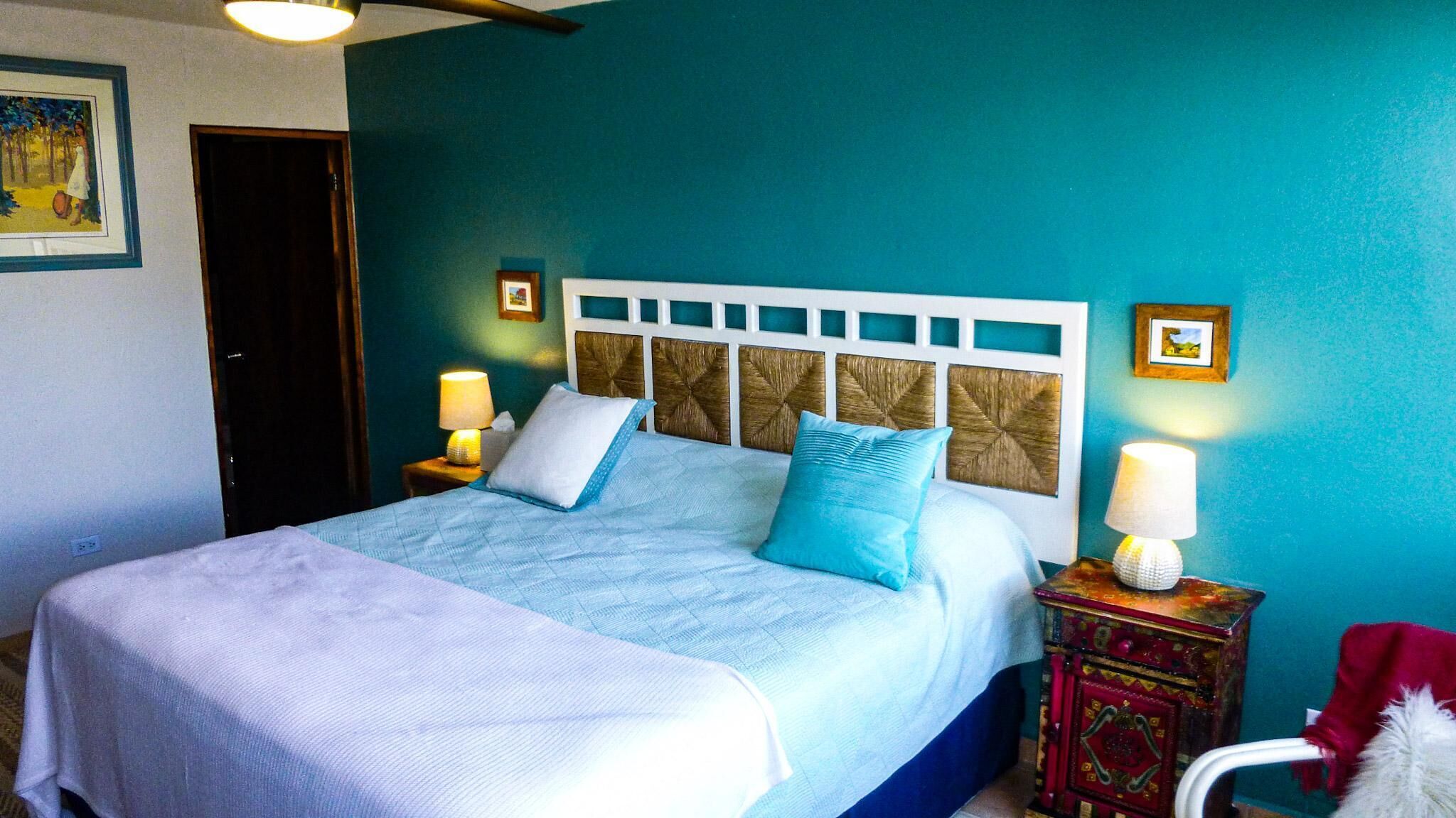 A bedroom with a bed, two bedside tables, a nightstand, a chair, and a door.
