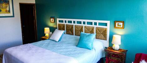 A bedroom with a bed, two bedside tables, a nightstand, a chair, and a door.