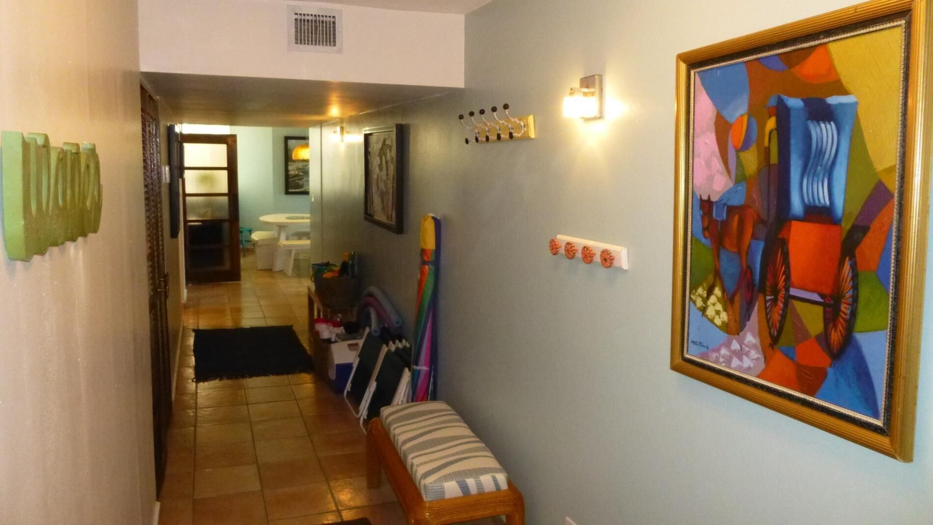 A hallway with a bench, a colorful abstract painting, and a coat rack.