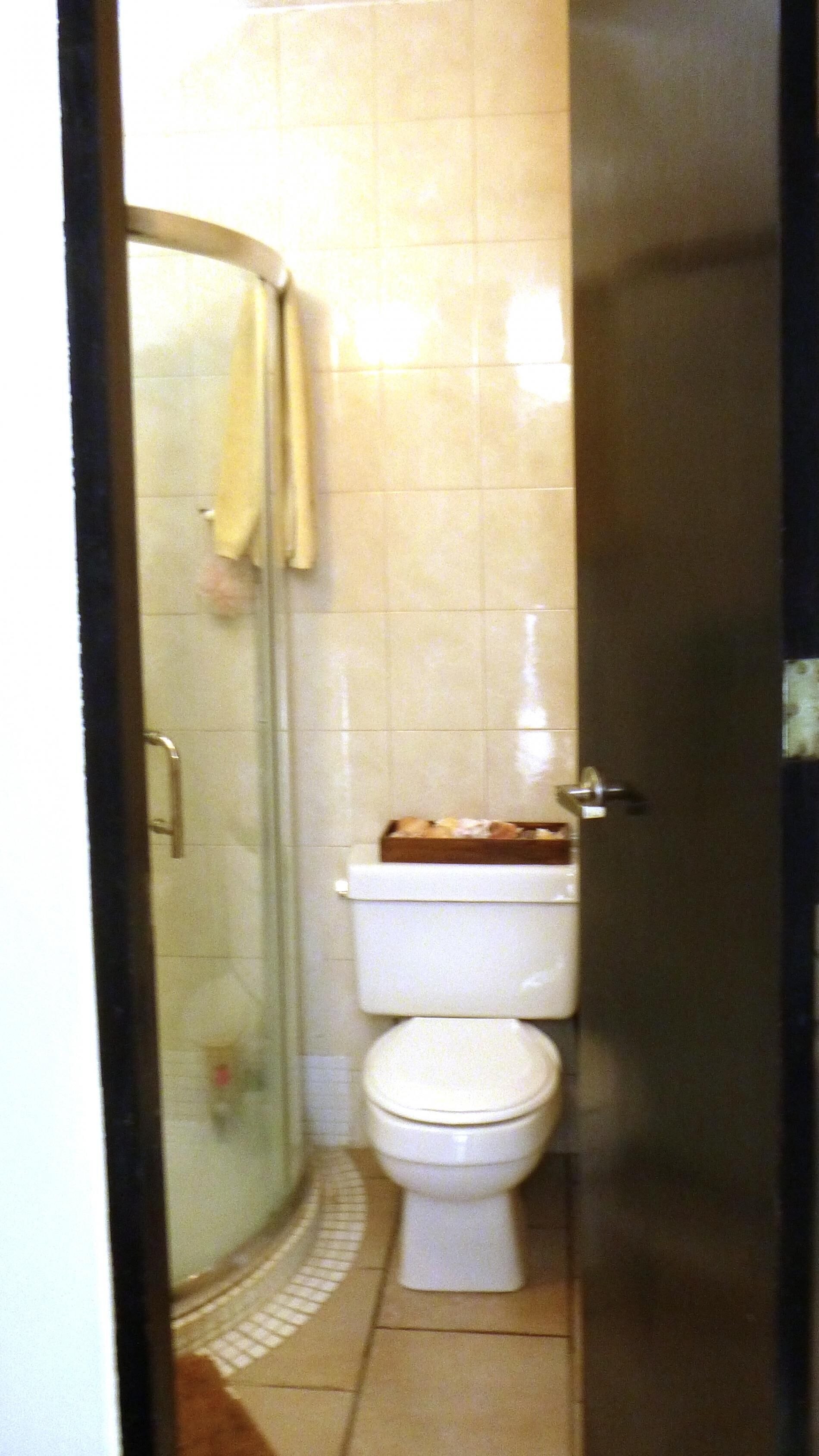 Une salle de bain avec une douche à parois de verre, des toilettes et un petit plateau en bois posé sur le réservoir des toilettes.