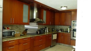 A kitchen with wooden cabinets, stainless steel appliances, granite countertops, and a tiled backsplash. - Casa Almendro (San Juan)
