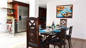 A dining area with a wooden table set for four, surrounded by chairs. A painting of boats on water hangs on the wall. - Casa Almendro (San Juan)