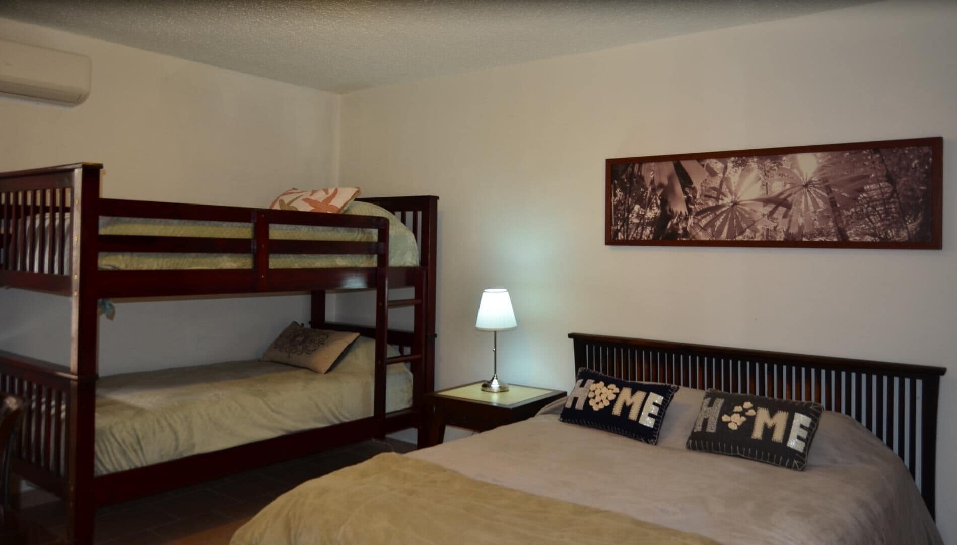 A room with a bunk bed, a single bed, a nightstand with a lamp, and a framed picture on the wall.