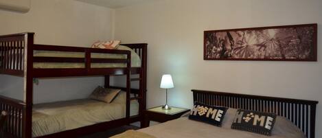 A room with a bunk bed, a single bed, a nightstand with a lamp, and a framed picture on the wall.