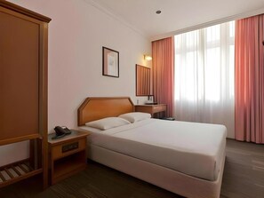 A hotel room with a large bed, a bedside table with a lamp, a wardrobe, and a window with curtains. - Penta Hotel (Singapore)