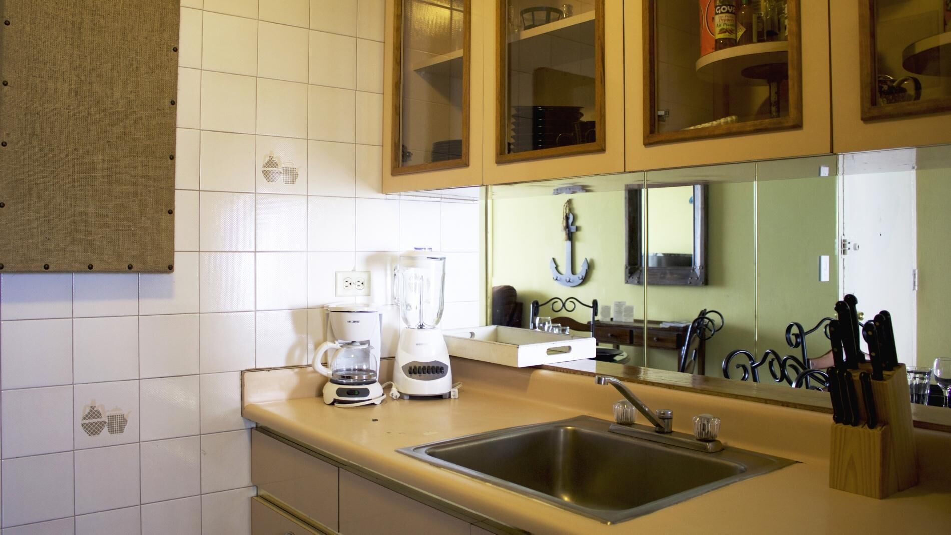 Una cucina con piastrelle bianche, una macchina da caffè, un frullatore, un lavandino e un portacoltelli.